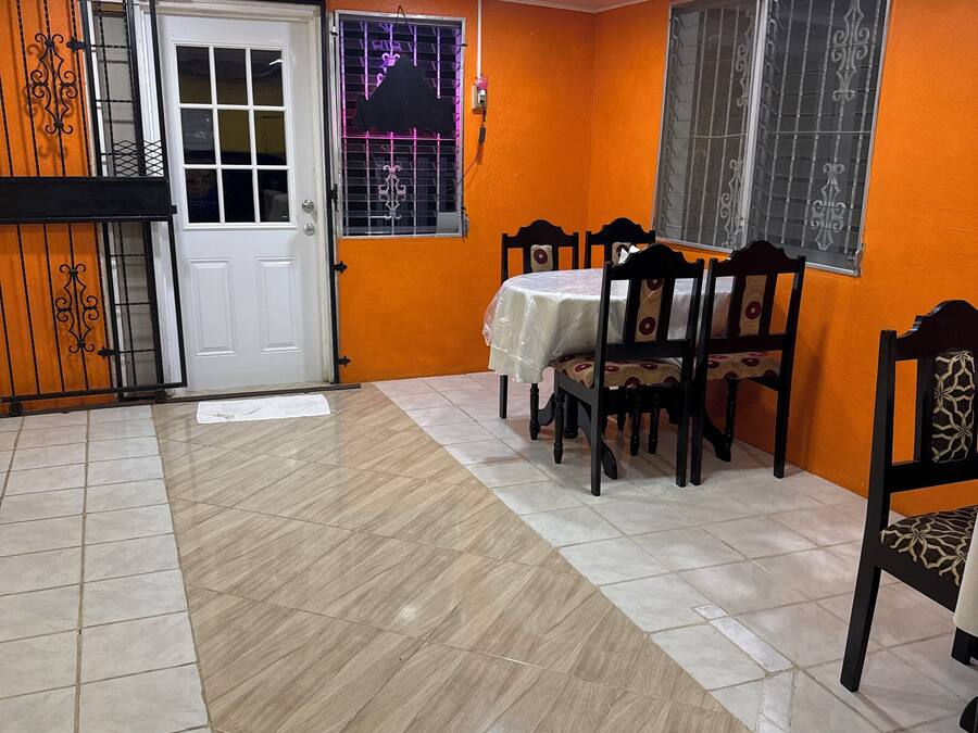 A dining area with a table and chairs, a door, and windows with metal bars.