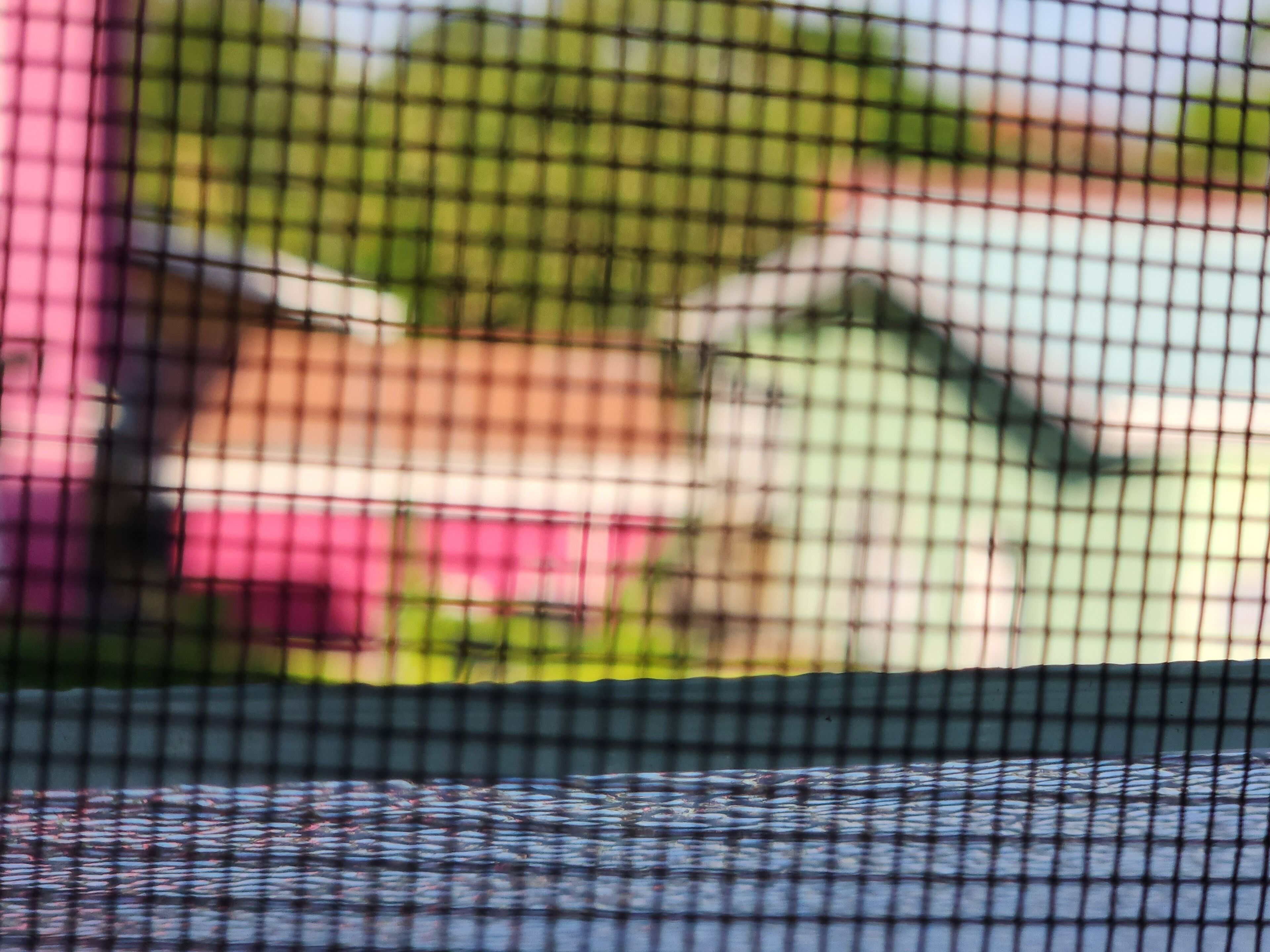 A blurred view of a building through a wire mesh, with indistinct shapes and colors.
