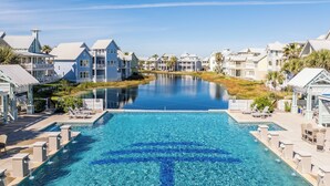 Une grande piscine à eau claire, de forme en T, entourée de villas en bord de mer et d’espaces de détente.