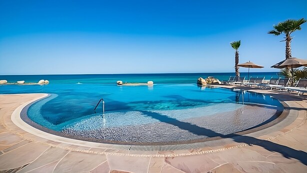 Ein Poolbereich mit klarem, blauem Wasser, Liegestühlen und Palmen.