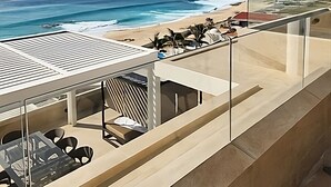 Ein Balkon mit Blick auf das Meer und den Strand, ausgestattet mit Sitzgelegenheiten im Freien und einer Glasumlaufung.