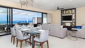 Ein modernes Wohnzimmer mit Essbereich, großen Fenstern, einem Deckenventilator und einem Flachbildfernseher.