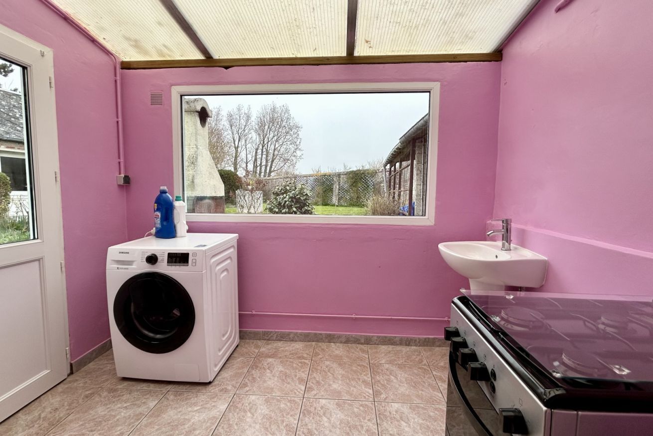 A laundry room with a washing machine, a sink, and a window with a view of a garden.