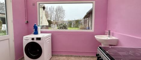 A laundry room with a washing machine, a sink, and a window with a view of a garden.