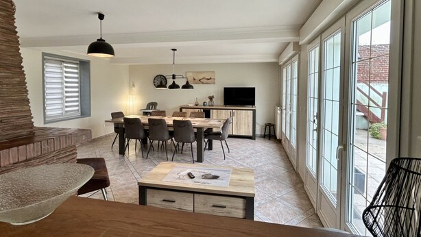 A modern kitchen with a dining area, large windows, and a TV.