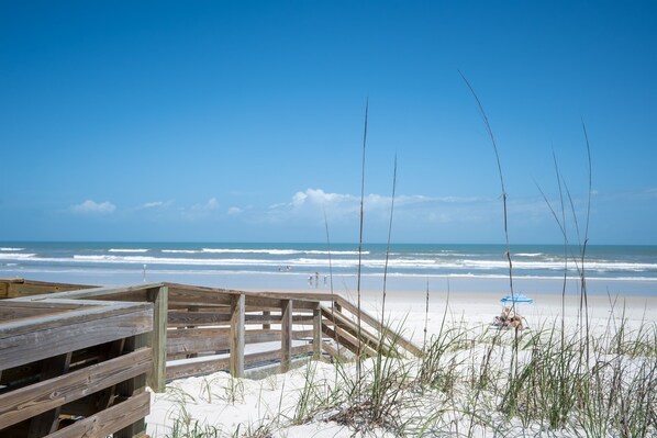 A wooden boardwalk leading to a sandy beach with a clear blue sky.