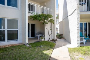 A residential building with a covered patio, a small tree, and outdoor seating.