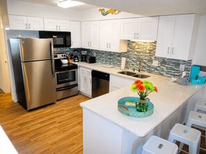 A modern kitchen with stainless steel appliances, white cabinetry, and a central island with a vase of flowers.