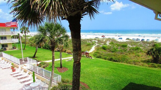 A view of a beachside property with a lawn, palm trees, and a view of the ocean. - Oceanfront End-Unit | Pool View, Washer/Dryer (St. Augustine Beach)