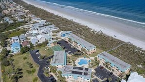 An aerial view of a coastal hotel with multiple buildings, a parking lot, and a beach in the background. - Ocean-View Condo | Pool + Balcony | Crescent Beach (St. Augustine Beach)