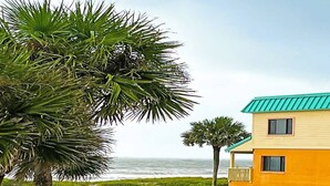 A coastal building with a green roof, surrounded by lush greenery and a view of the ocean. - Ocean-View Condo | Pool + Balcony | Crescent Beach (St. Augustine Beach)