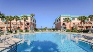 A swimming pool surrounded by two-story buildings with balconies, palm trees, and lounge chairs. - Ocean-View Condo | Pool + Balcony | Crescent Beach (St. Augustine Beach)