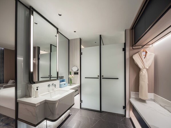 A modern bathroom with a large mirror, dual sinks, a glass shower enclosure, and a robe hanging on the wall.