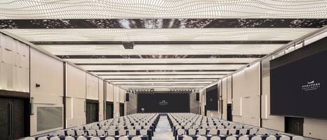 A conference room with rows of chairs, a stage, and a large screen.