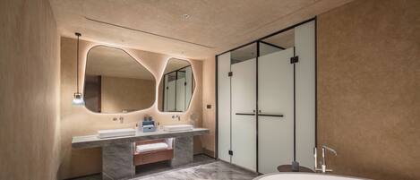 A modern bathroom with a large bathtub, two sinks with marble countertops, and a large mirror with an abstract design.