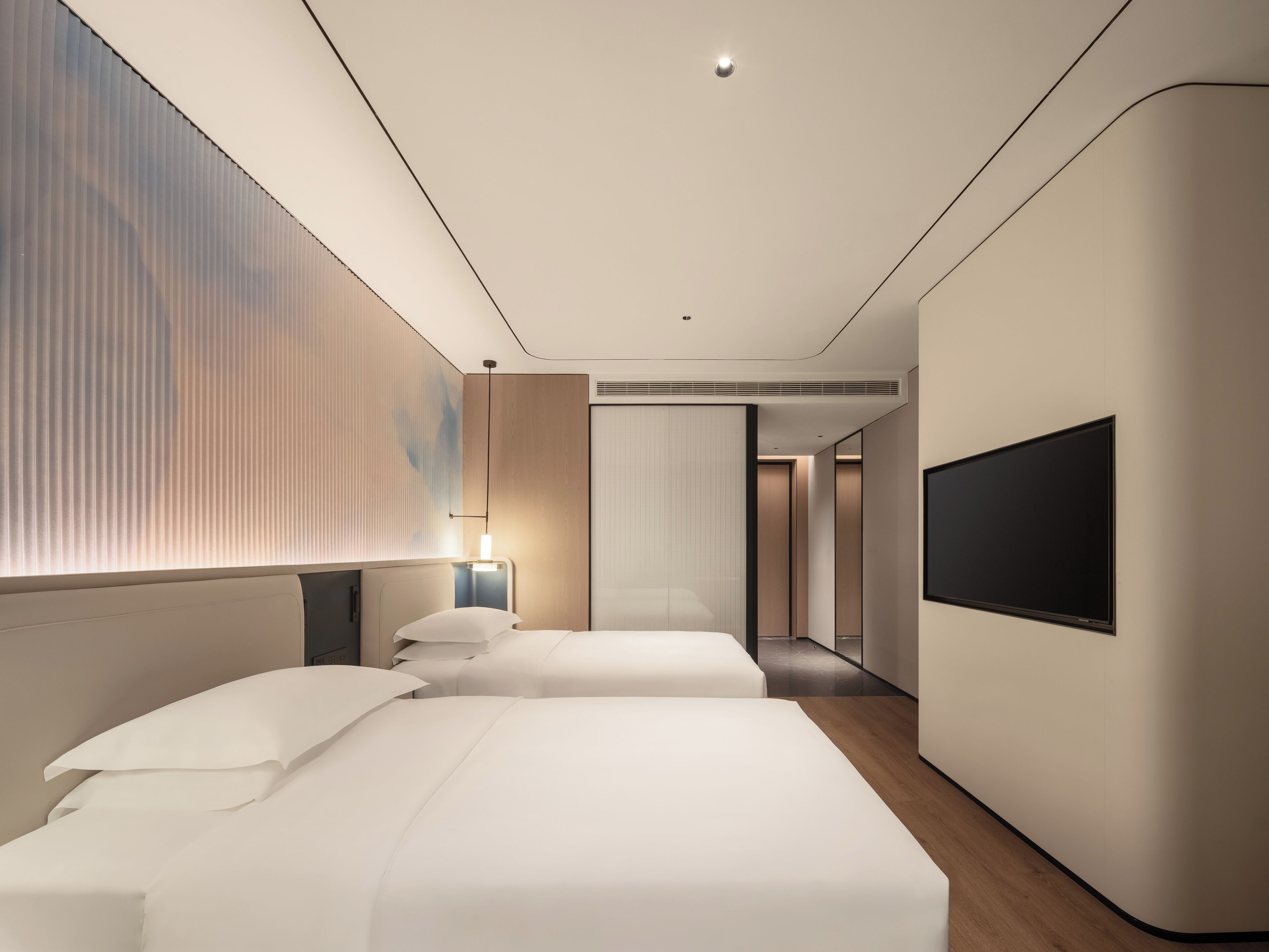 A modern hotel room with two beds, a flat-screen TV, and a large window with blinds.