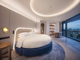 A modern hotel room with a large bed, a desk, and a view of the city.