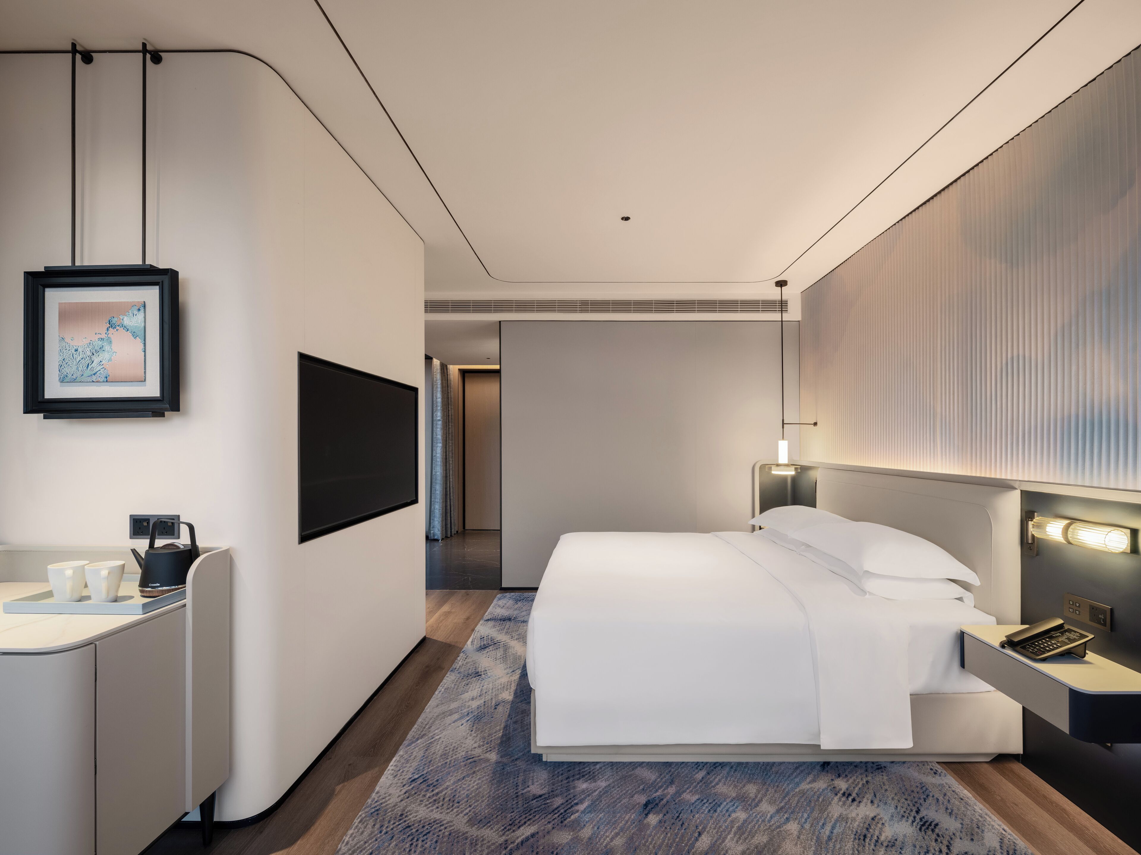 A modern hotel room with a bed, bedside table, lamp, and a framed picture on the wall.