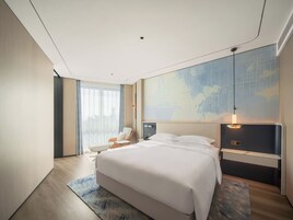 A modern hotel room with a large bed, a seating area with a chair, a desk, and a world map on the wall.