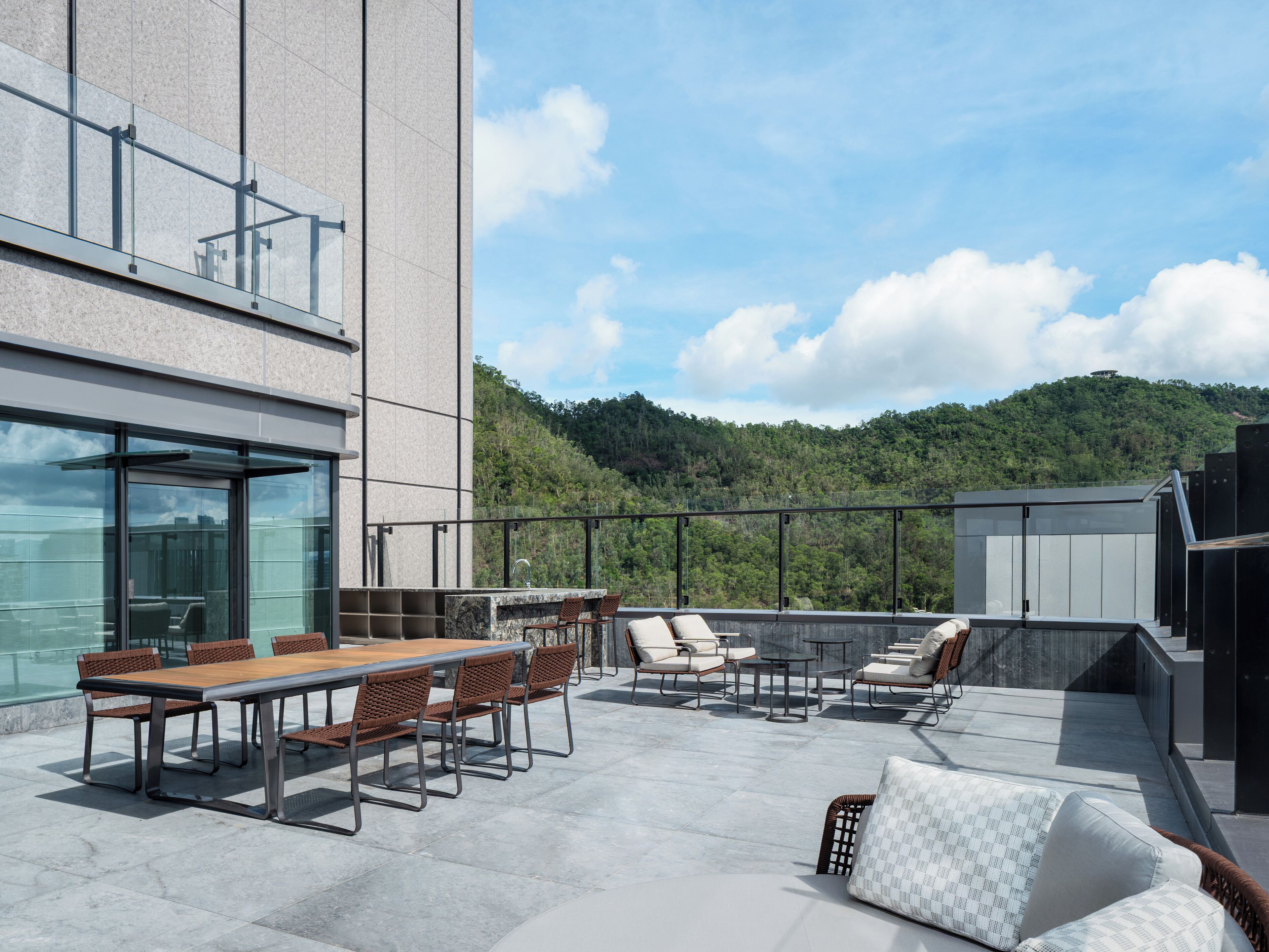 Terraza en la azotea con comedor, asientos y vistas a una colina boscosa.