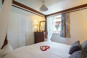 Ein Schlafzimmer mit einem Bett, einem Schminktisch, einem Spiegel und einem Fenster mit Vorhängen.