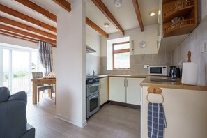 Eine moderne Küche mit Holzbalken, einem Essbereich mit Tisch und Stühlen sowie einem Ausblick durch ein Fenster.