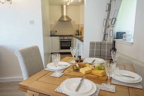 Une table à manger dressée avec des assiettes, des couverts, des verres, ainsi qu’un assortiment de fromages et d’olives.