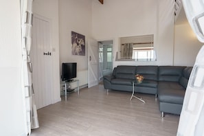 Un salon avec un canapé gris, une table basse en verre, un téléviseur à écran plat et un tableau accroché au mur.