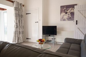 A living room with a sofa, a glass table with fruit, a television, and a door with a curtain.