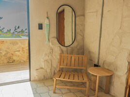 A room with a wooden bench, a small round table, a mirror, and a view of the outside.