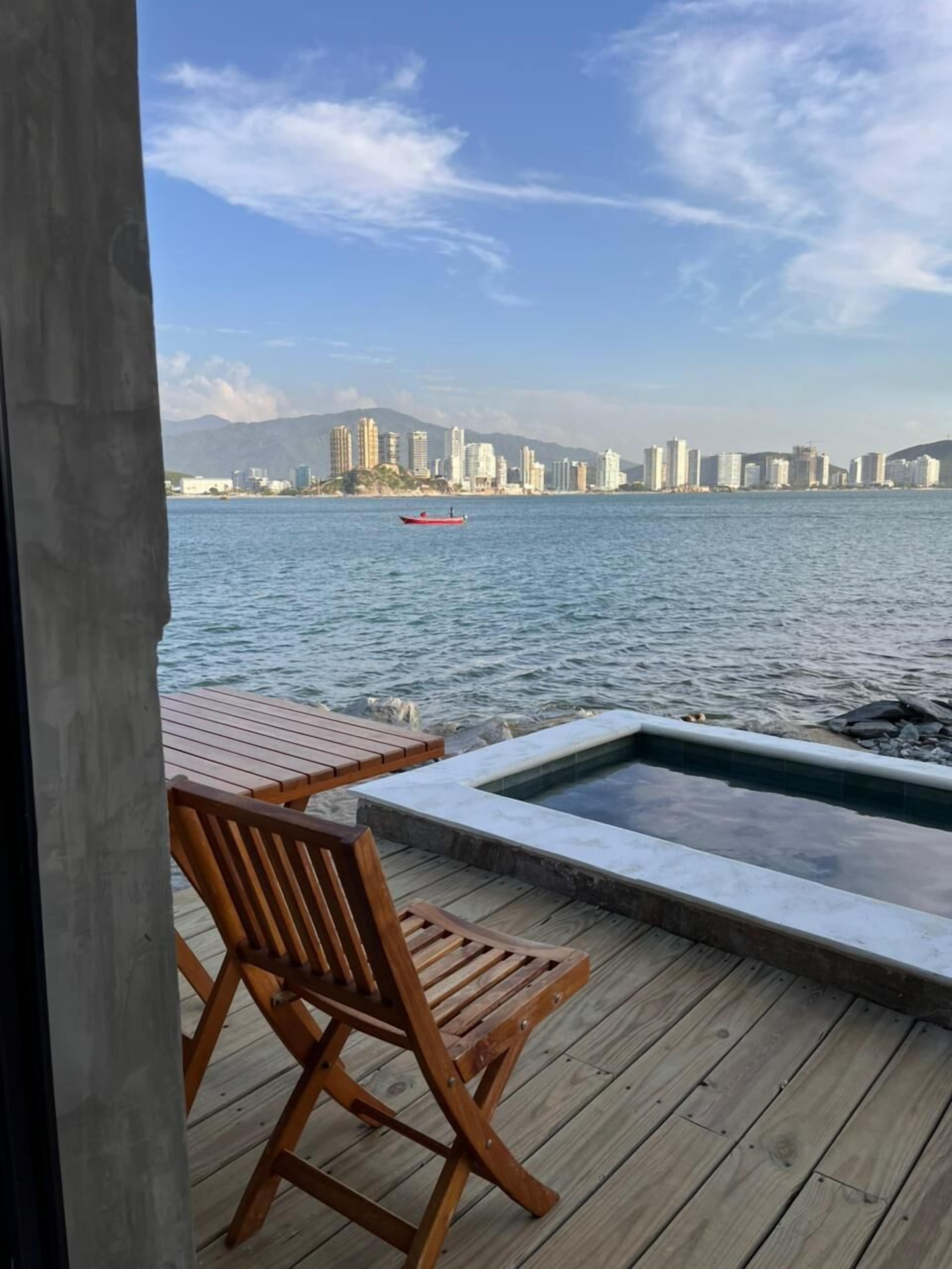 A wooden deck with a pool and a view of a city skyline across a body of water.