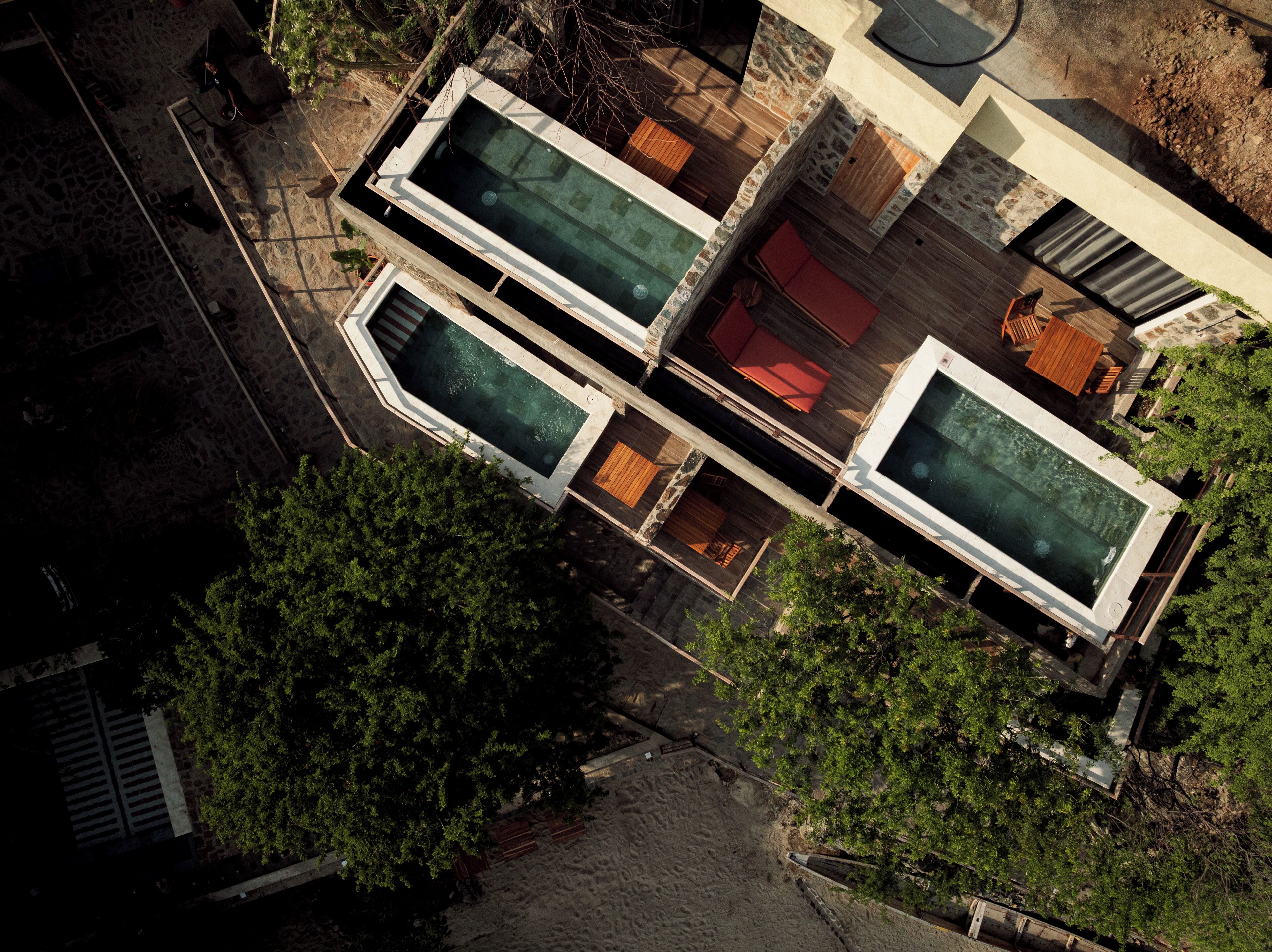 An aerial view of a modern building with two rectangular swimming pools, a stone patio, and surrounding greenery.