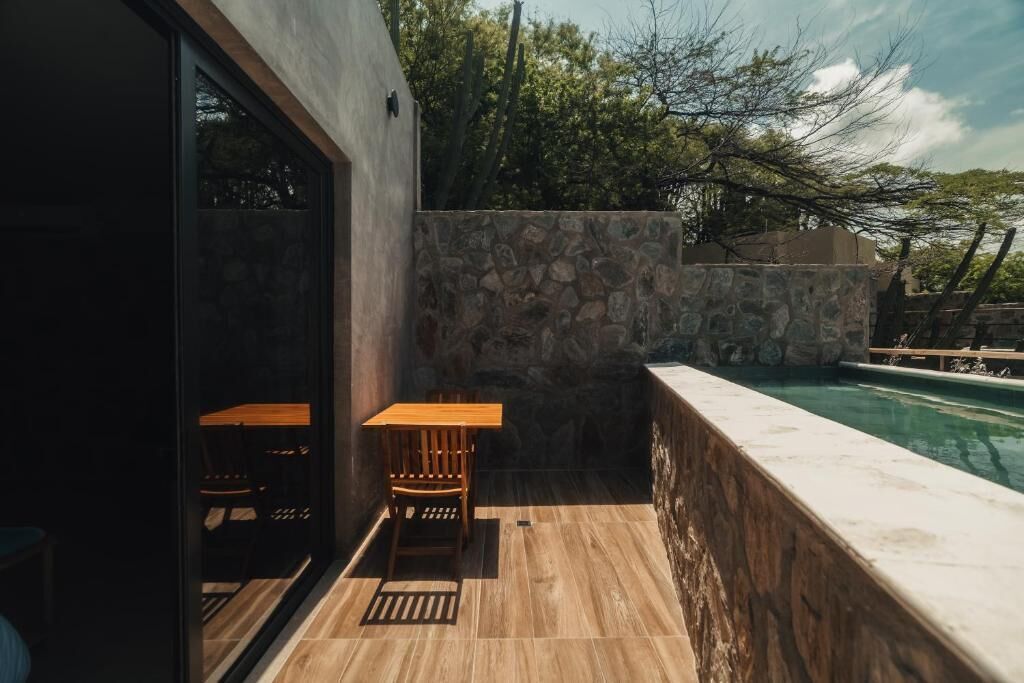 A patio with a stone wall, a wooden table, and a pool.