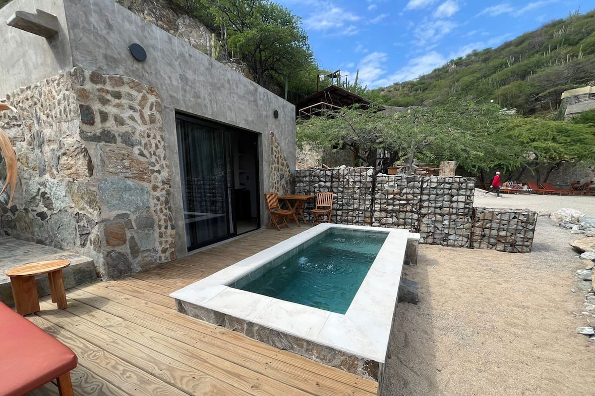 A stone building with a pool, wooden deck, and outdoor seating.