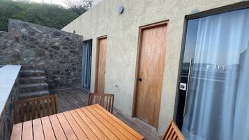 A patio with a wooden table and chairs, a stone wall, and a door leading to a covered area.