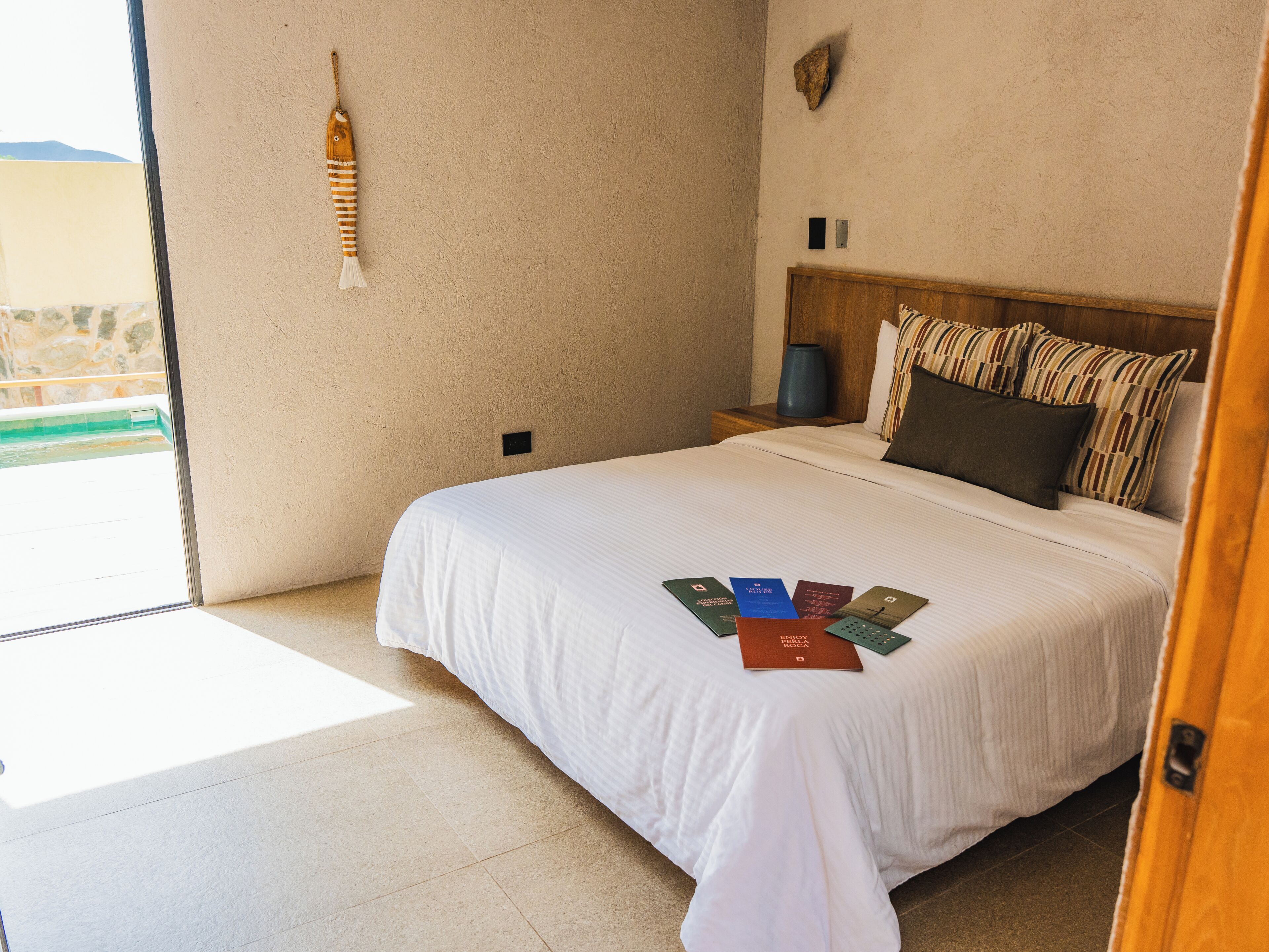 A hotel room with a bed, a nightstand, a lamp, and a view of the outside.