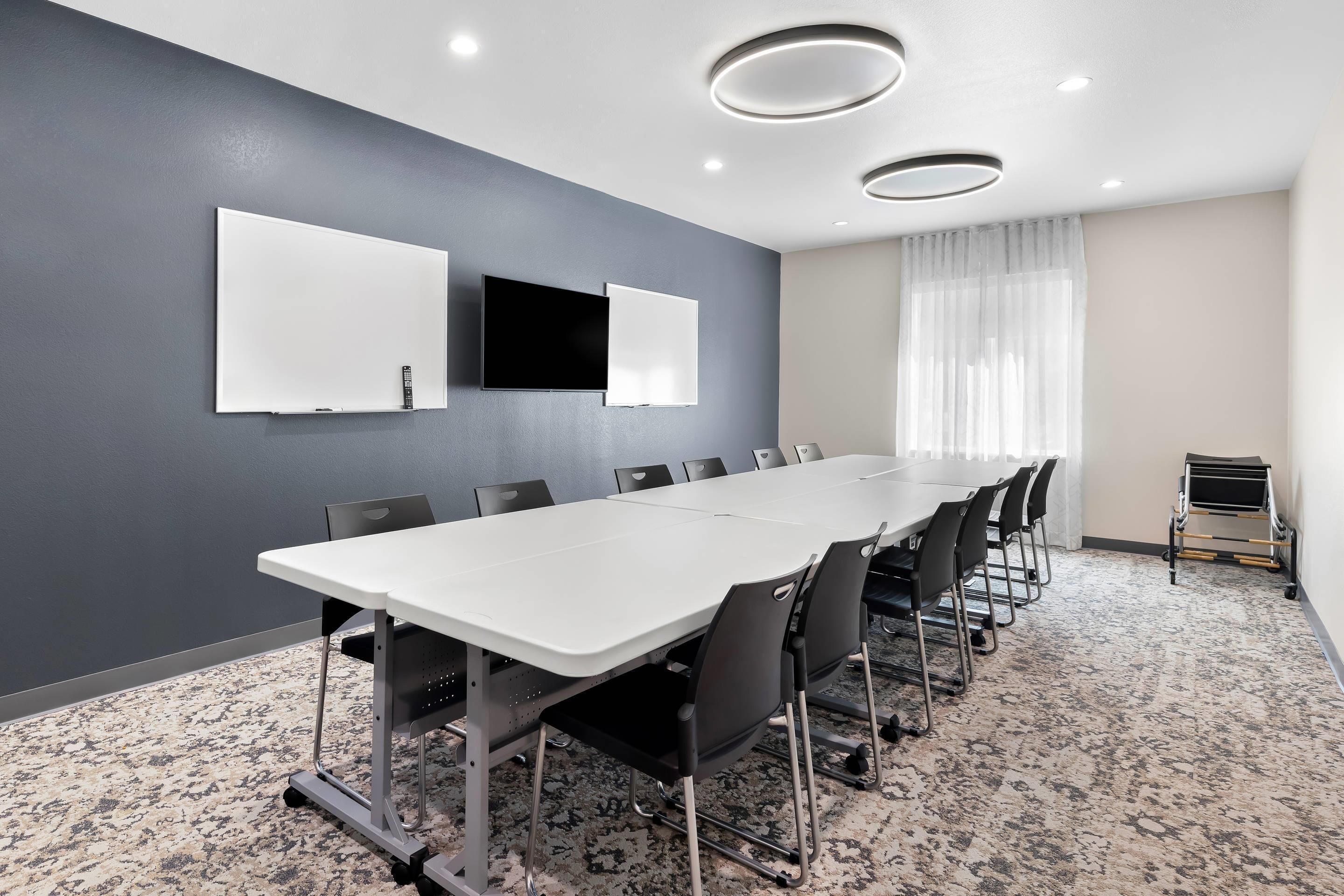 A conference room with a long table, chairs, a flat-screen TV, and a projector.