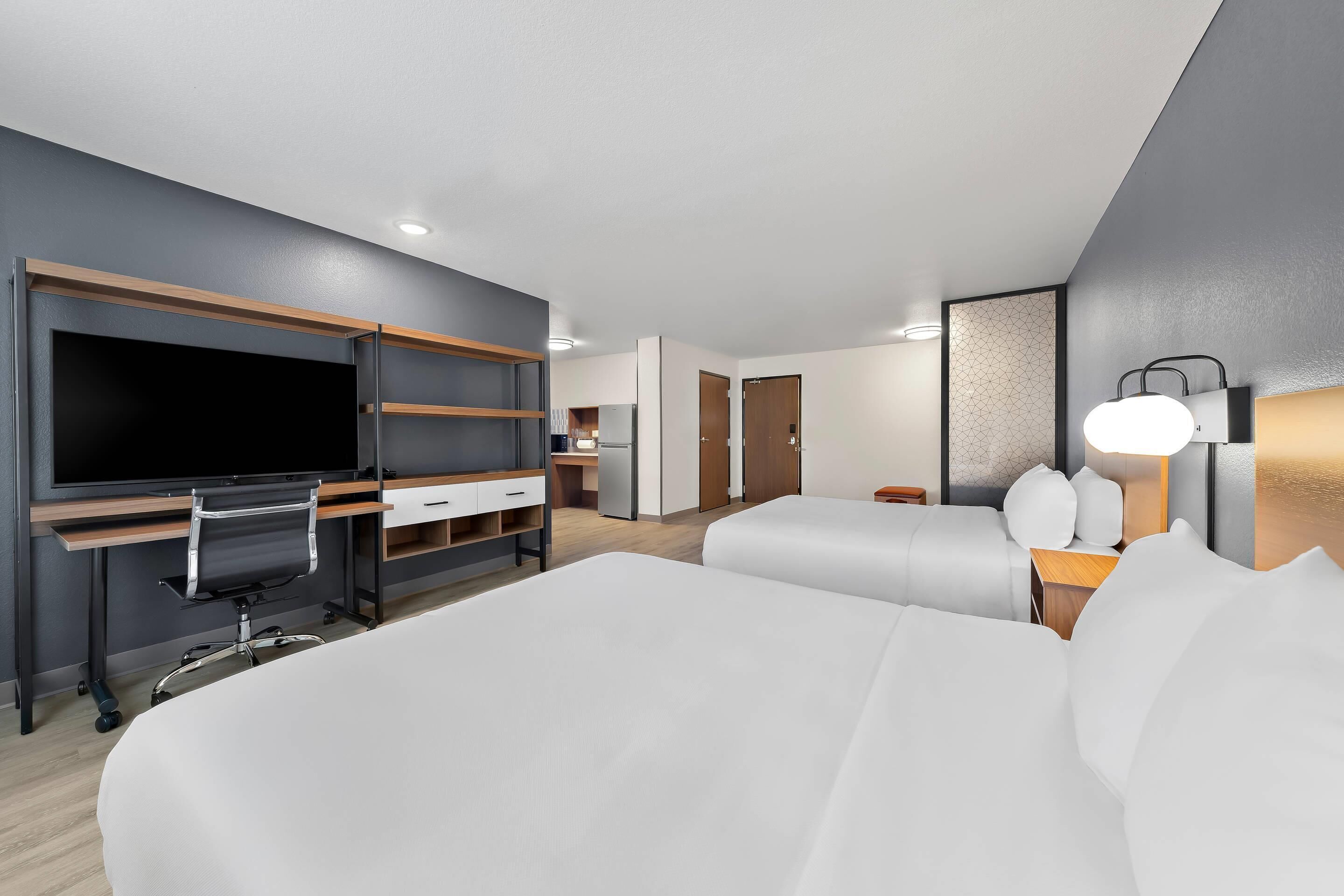 Une chambre d’hôtel moderne dotée d’un grand lit, d’un bureau avec un téléviseur à écran plat, d’une table de chevet avec une lampe et d’une armoire.