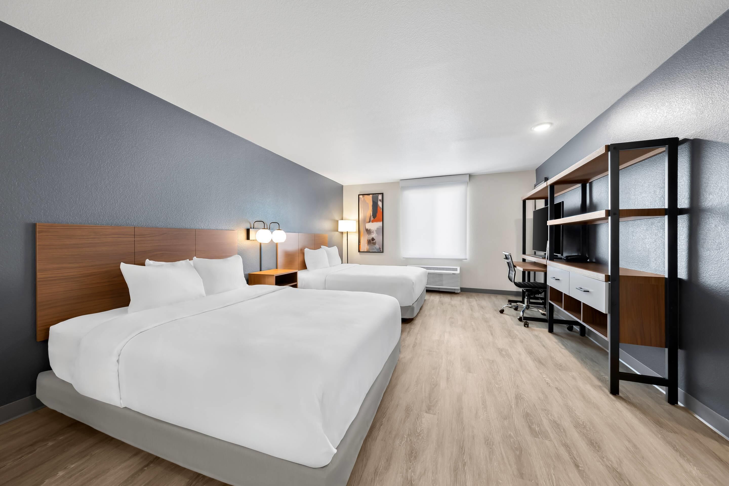 Hotellihuone, jossa on kaksi sänkyä, työpöytä, tuoli ja suuri ikkuna.