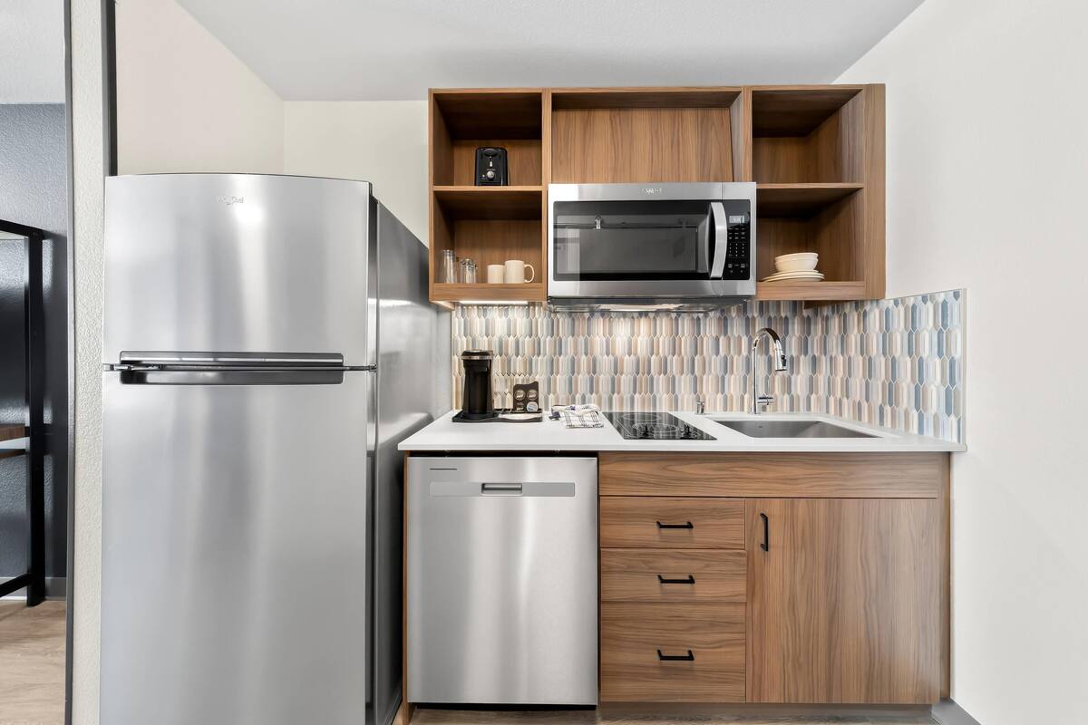 Une cuisine moderne équipée d’un réfrigérateur en acier inoxydable, d’un four à micro-ondes et de meubles de rangement en bois.