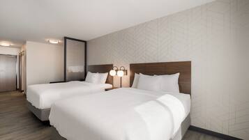 Une chambre d’hôtel avec deux lits, une tête de lit en bois, un luminaire fixé au mur et un mur orné d’un motif géométrique.