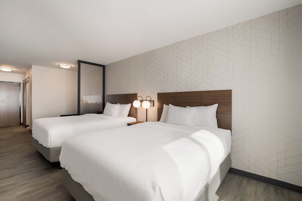 Habitación de hotel con dos camas, cabecero de madera, lámpara de pared y pared con un motivo geométrico.