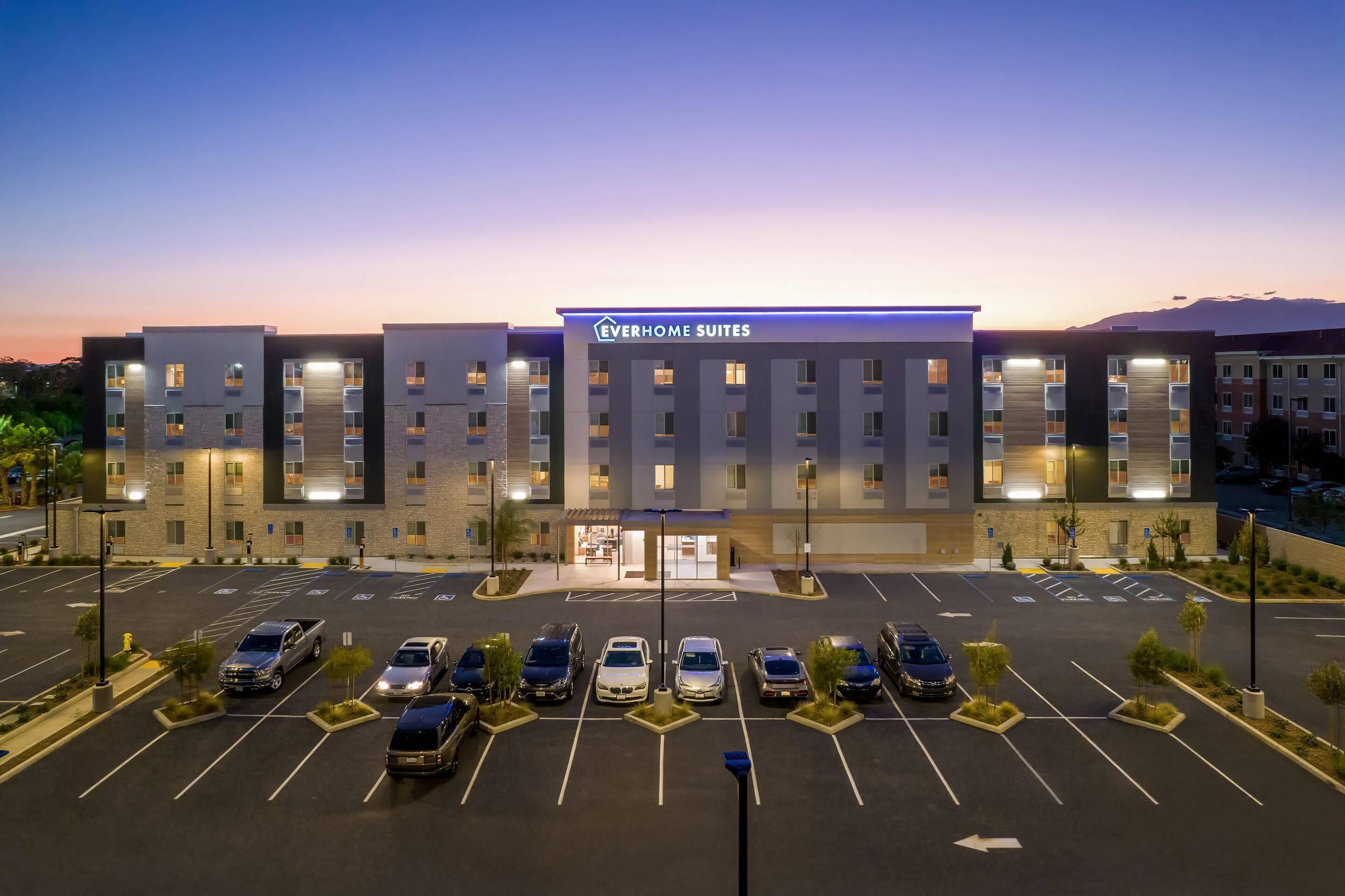 Un hôtel au design moderne, de la chaîne « Everhome Suites », doté d’un parking pouvant accueillir de nombreux véhicules et offrant une vue sur un ciel dégagé.