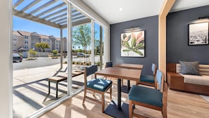 A modern interior with a dining area, a sofa, and a large window offering a view of the street.