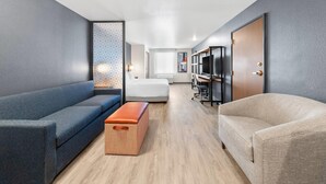 A modern hotel room with a sofa, a bench, a TV, and a bed. - Everhome Suites San Bernardino - Loma Linda (San Bernardino)