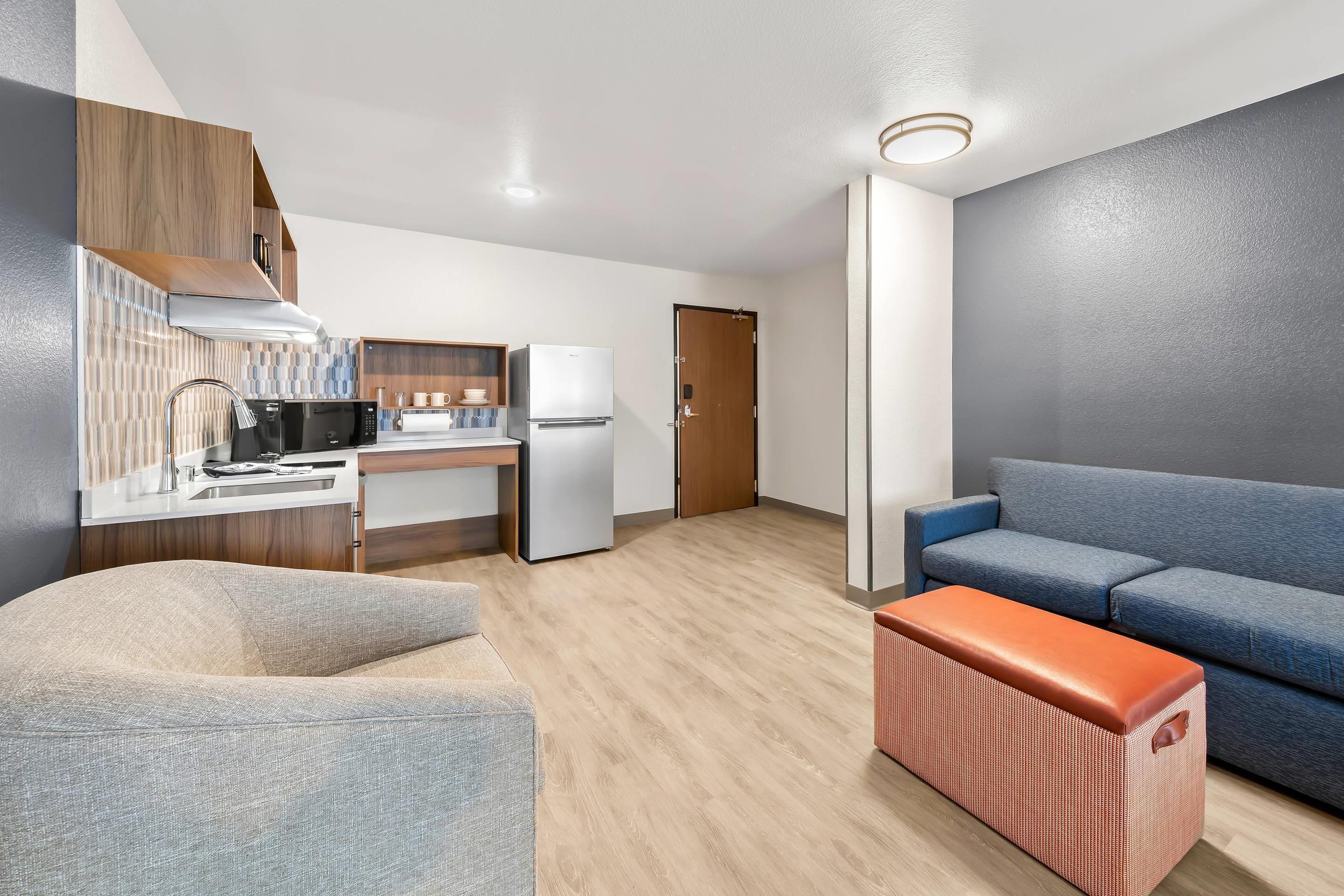 Een moderne woonkamer met een bank, een salontafel en een keukenhoek met een magnetron en een koelkast.