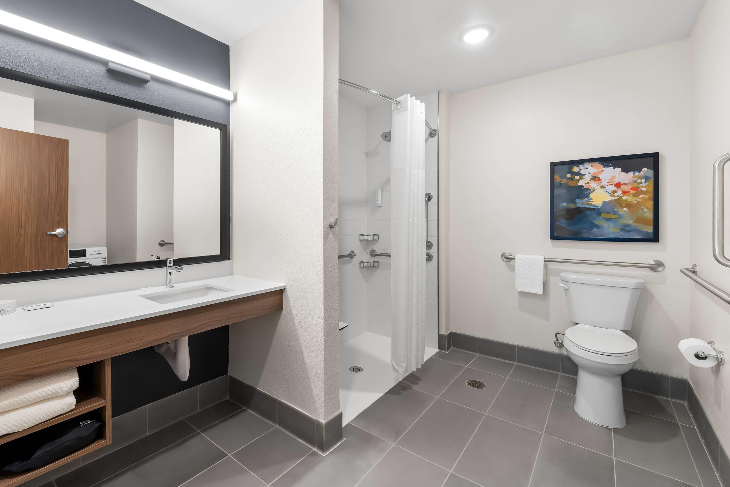 Un baño moderno con lavamanos, espejo e inodoro blancos.