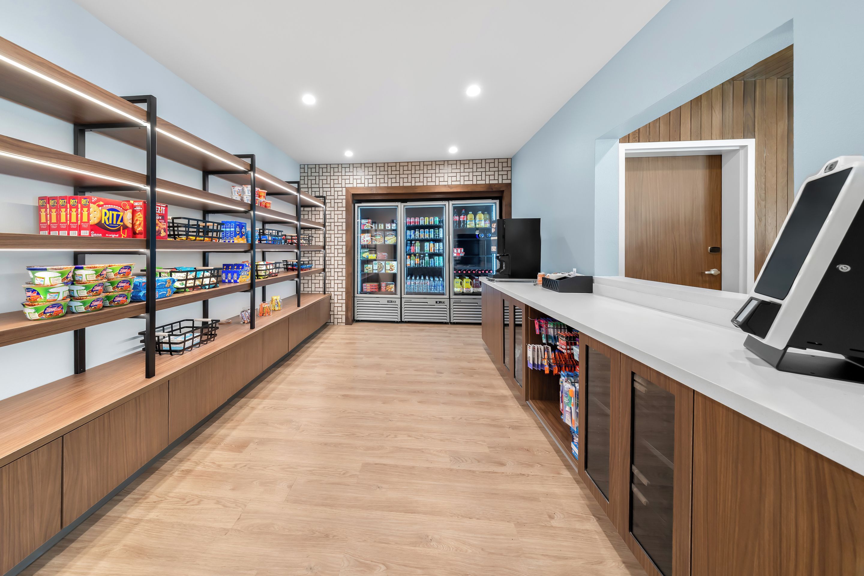 A clean, modern grocery store interior with wooden flooring, metal shelving, and refrigerated sections.