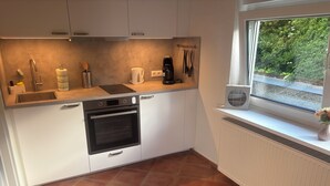 A modern kitchen with white cabinets, a built-in oven, a coffee maker, and a window with a view of greenery. - Cozy apartment directly on the Rhine (Wiesbaden)