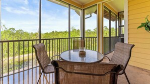 A balcony with wicker furniture and a glass table, overlooking a natural landscape.